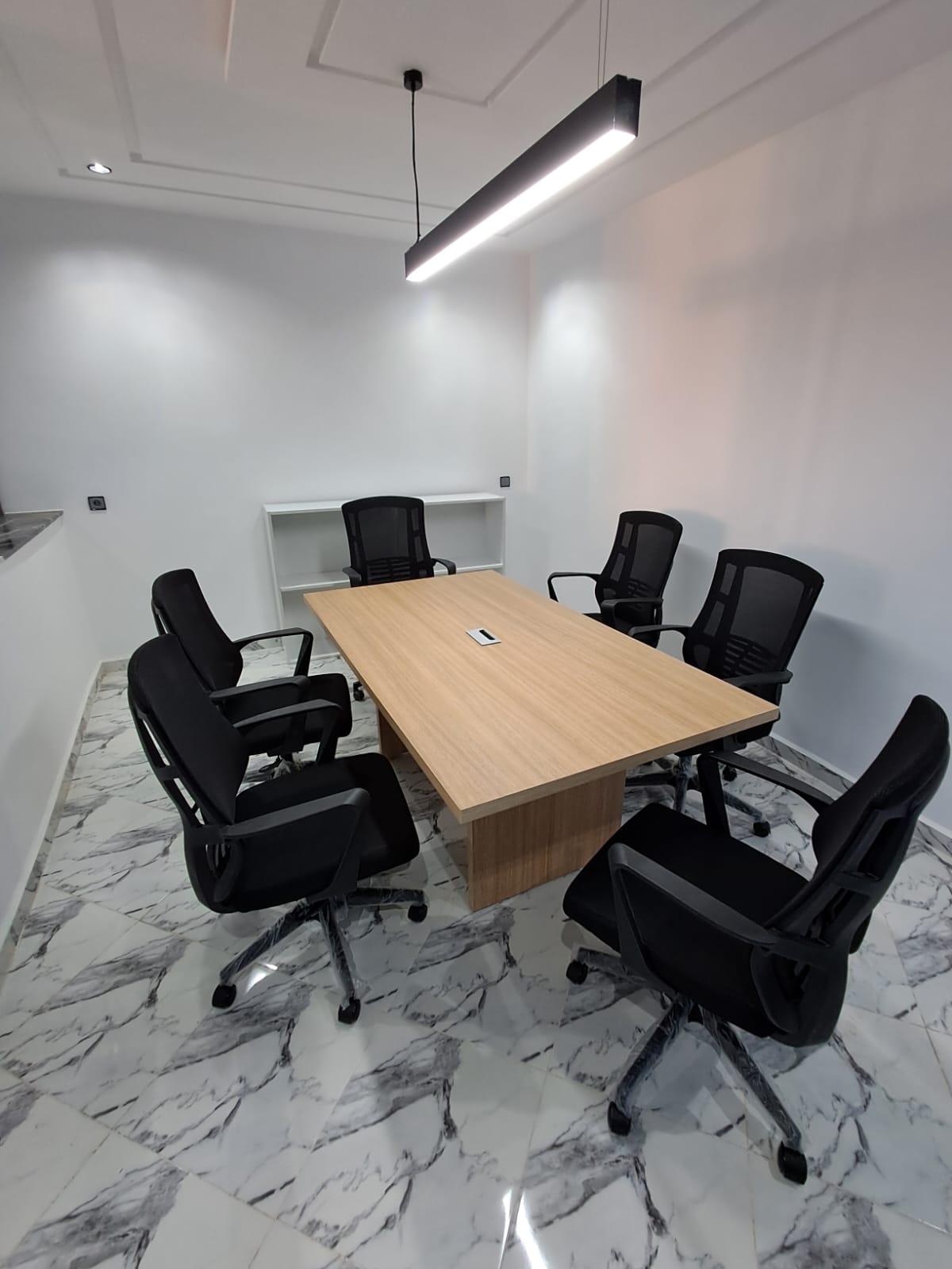 Table de réunion bois et chaises noires sous un éclairage suspendu.
