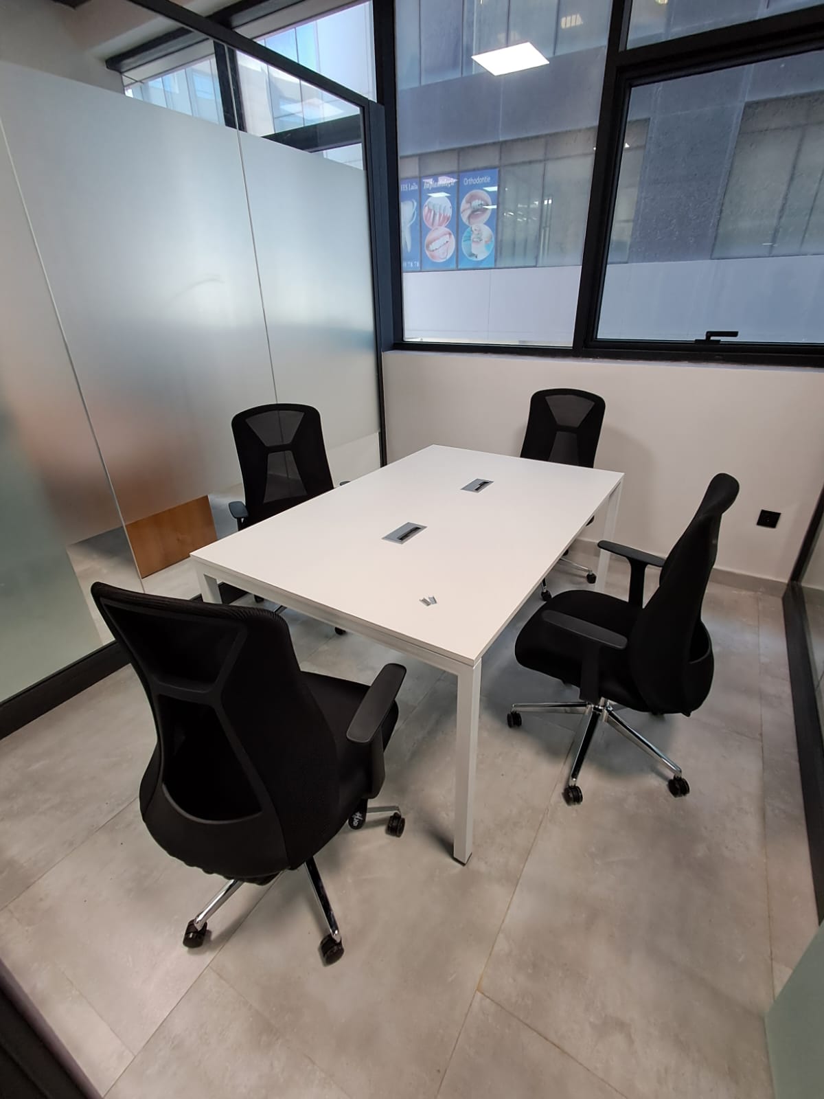 Table de réunion blanche et chaises noires dans un bureau vitré.